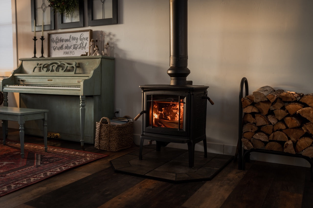 Living room with a fire in wood burning stove that has a draw collar installed on the stove pipe.