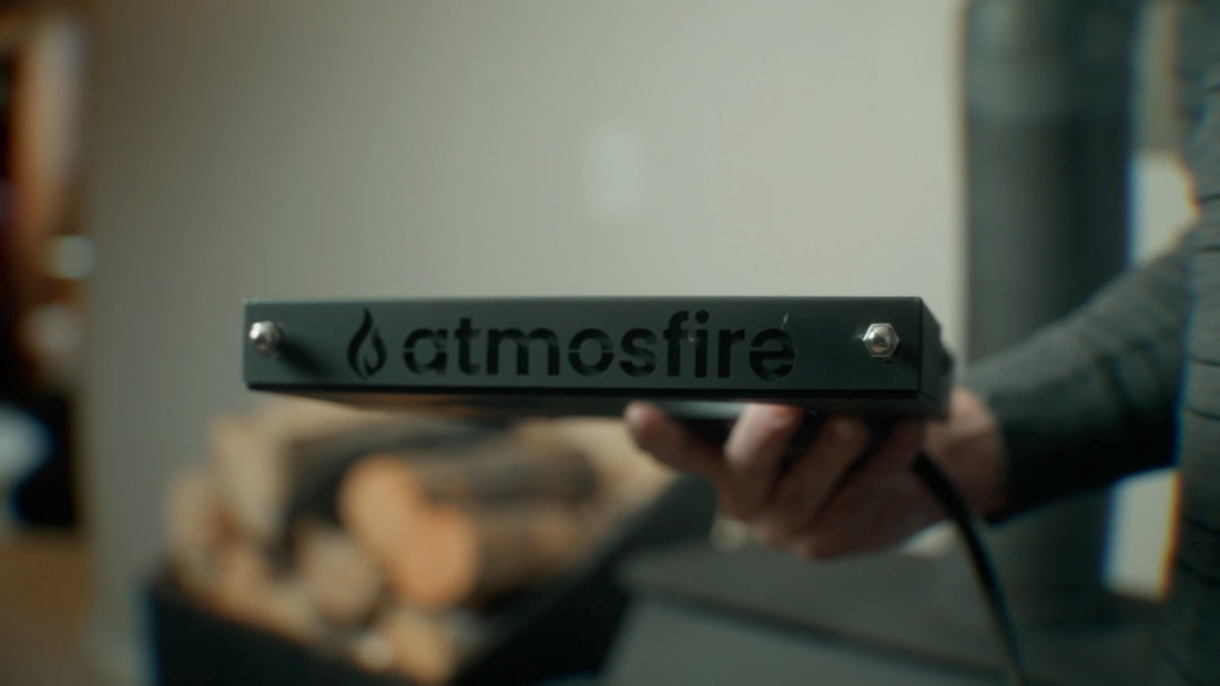 Close up of air damper with engraved "Atmosfire" on the front with firewood and wood burning stove in the background.